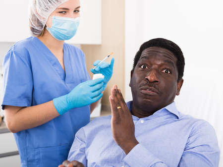 Afro american male patient feeling frightened of skin care injectionの写真素材