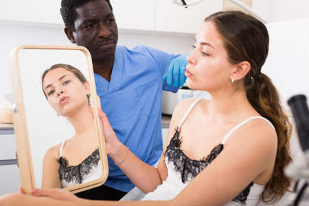 Woman looking at mirror while cosmetician explaining facial procedureの写真素材