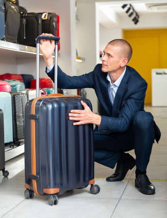 Focused young man carefully examines a travel suitcaseの写真素材
