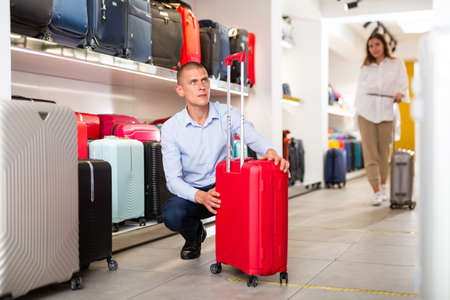Focused young man carefully examines a travel suitcaseの写真素材