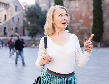 Portrait of mature cheerful woman in white blouse standing on a old city street