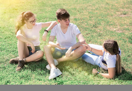 Group of teenagers chatting while sitting on green lawnの写真素材
