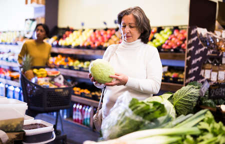 Mature woman choice cabbage on grocery store shelvesの写真素材