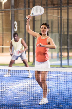 Woman playing padel in a green grass padel court indoor behind netの写真素材