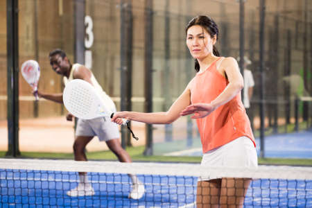 Woman playing padel in a green grass padel court indoor behind netの写真素材
