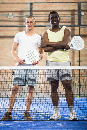 Two men with rackets in their hands chatting after playing padel on tennis courtの写真素材