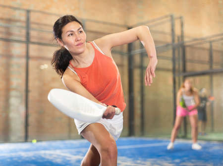Woman playing padel in a green grass padel court indoor behind netの写真素材