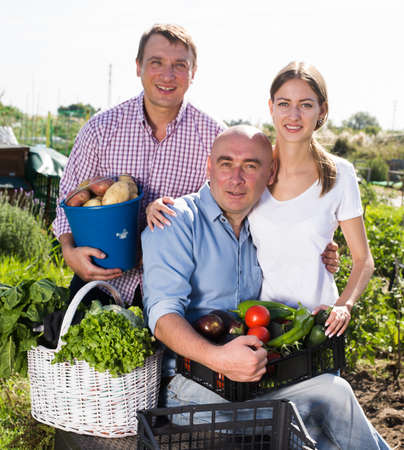 Family of three gardeners posing with harvest of vegetables and greensの写真素材