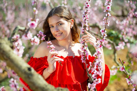 Lady wearing red dress and posing in park with blooming treesの写真素材