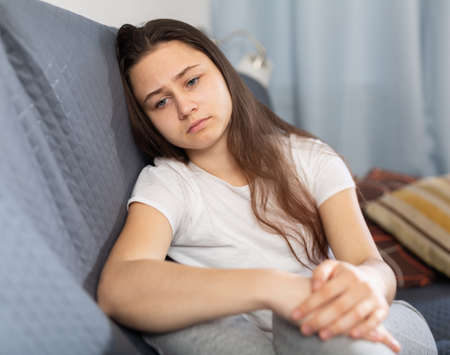 Depressed young woman sitting on sofa at homeの写真素材