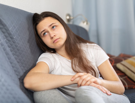 Depressed young woman sitting on sofa at homeの写真素材