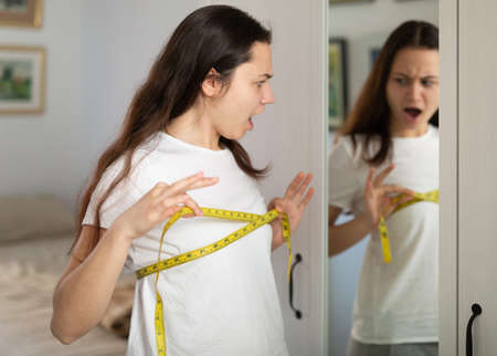 Sad young pretty woman measuring breastsの写真素材