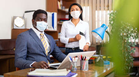Two business colleagues in protective masks in office interiorの写真素材
