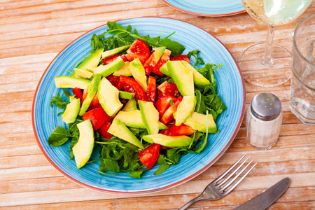 Tasty salad with avocado, tomatoe and arugula at plate