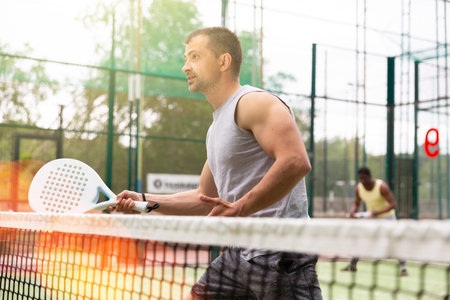 Male players playing padel in a padel court outdoor behind net