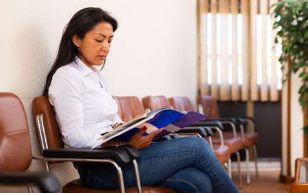 Focused Hispanic female entrepreneur reading documents in office hallの写真素材