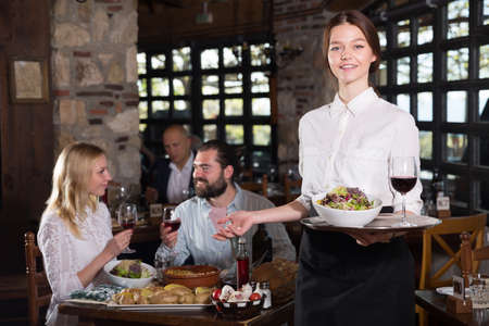 Professional waitress greeting customers at table in rustic restaurantの写真素材