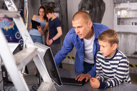 Young man with tween son using computer in escape roomの写真素材
