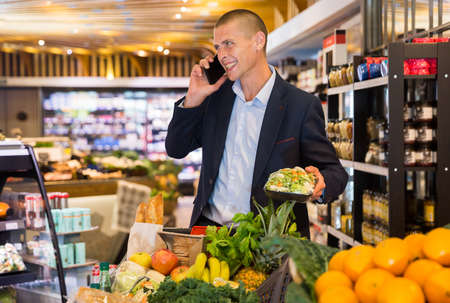 Young focused man using phone during shoppingの写真素材