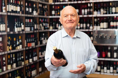 Elderly man chooses red wine in a liquor storeの写真素材