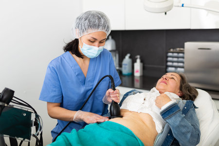 Professional woman cosmetician performing lifting procedure to mature woman on modern equipment in...