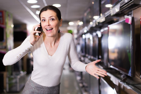Positive woman chooses TV set, talking by phone