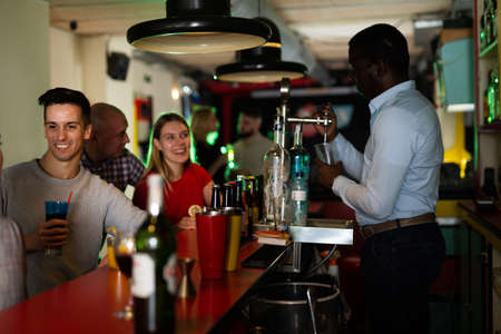 Young people with cocktails in hands chatting near the bar in nightclubの写真素材
