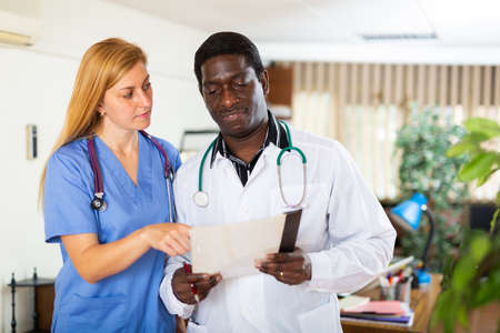 Two multinational doctors in the clinic discuss work issues while standing in an officeの写真素材
