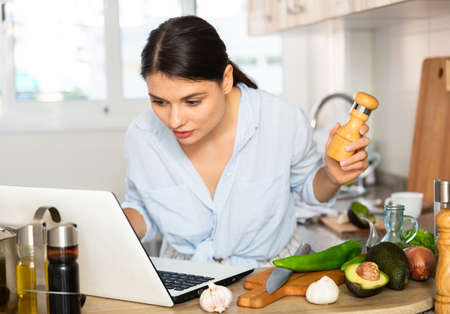 Nice woman planning to cook, looking for recipe on internet in her kitchenの写真素材