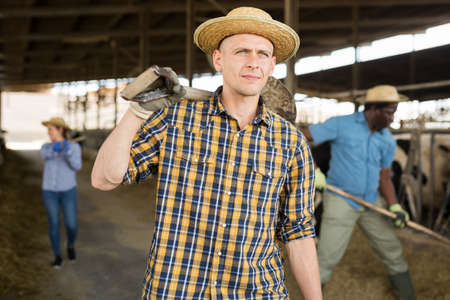 Portrait of a confident young male farmer standing in a cowshed with a shovelの写真素材
