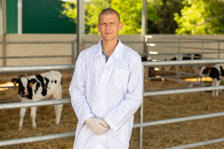 Portrait of male veterinarian who is standing at her workplace near cows at farm outdoors