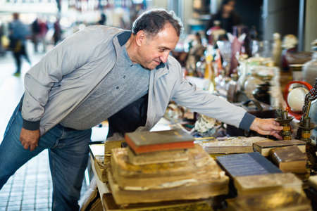 Positive elderly man choosing interesting souvenirs at traditional flea marketの写真素材