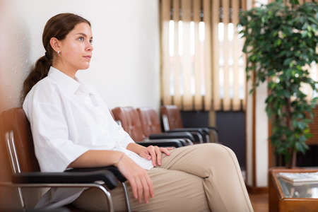 Woman sits on chair while waiting for reception in company officeの写真素材