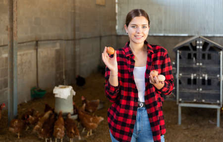Happy girl standing in hen house with chicken eggs in handsの写真素材