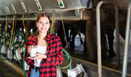 Female milker posing with glass of milk on dairy farmの写真素材