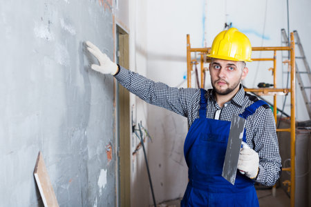 Adult male is checking the quality of the work done after the plaster wall