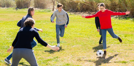 Company of teenagers playing football in park