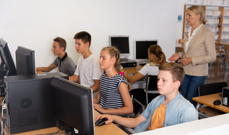 Schoolchildren using computers and teacher teaching them