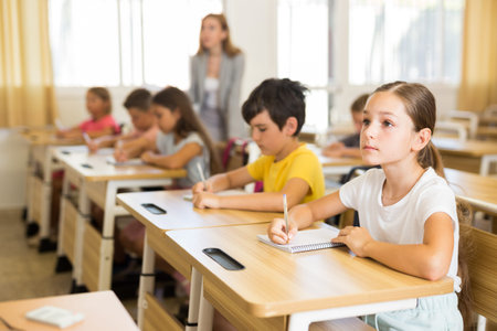 Diligent tween schoolgirl making notes of teacher lecture