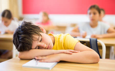 Bored tween boy sleeping at desk in classroom during lessonの写真素材
