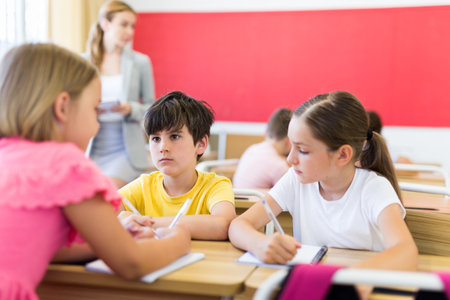 Interested preteen pupils discussing learning material in groupsの写真素材