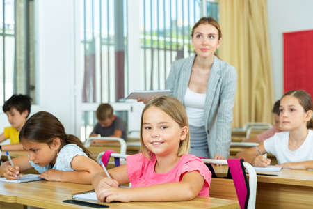 Two positive small school girls sitting together in classroomの写真素材