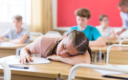 Tired teenage girl sleeping at desk in classroom during lessonの写真素材