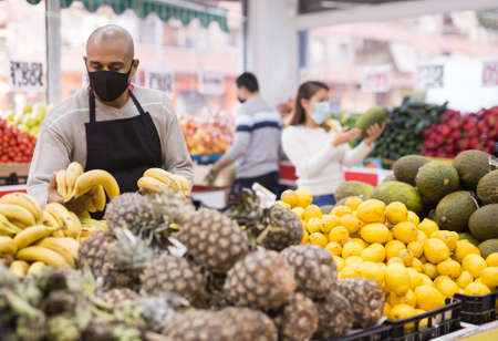 Friendly grocery store in protective mask employee lays ripe bananas on counterの写真素材