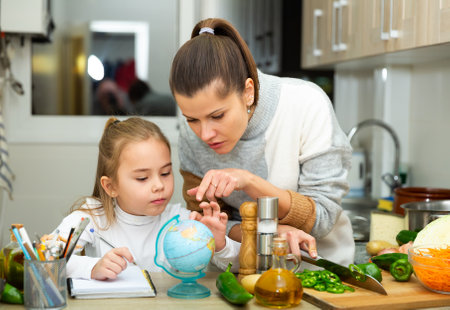 Mother cooking and little daughter doing school homeworkの写真素材