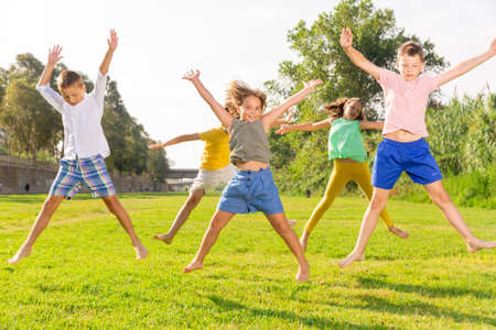 Cheerful preteen girls and boys jumping in summer city parkの写真素材