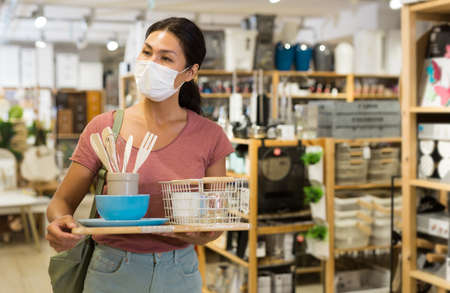 Female customer in protective mask holding purchases and walking in household goods storeの写真素材
