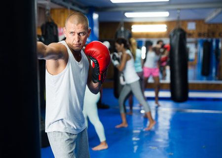 Young man in boxing gloves practicing punches on punchbag in gym