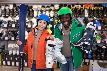 Portrait of cheerful couple posing in full skiing gear during shopping in sport goods storeの写真素材