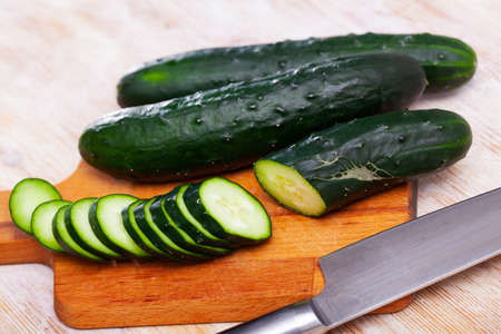Ripe cucumbers and knife on wooden cutting boardの写真素材